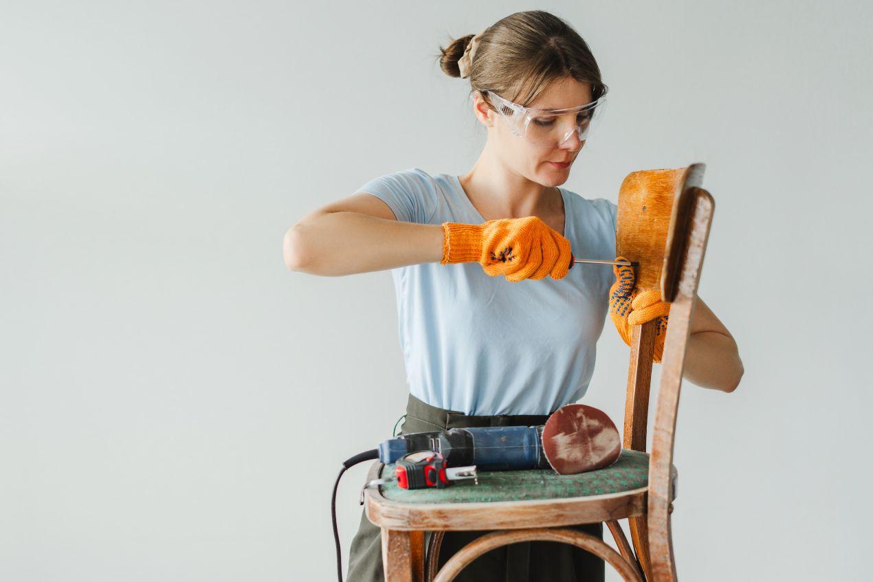 Frau schleift alten Stuhl für Möbel-Upcycling während der Wohnungssanierung in Berlin.