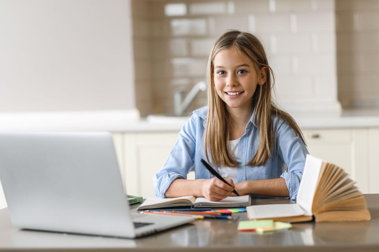 Mädchen sitzt am Tisch mit Laptop, Stift und Buch, konzentriert beim Mathelernen – optimale Lernumgebung für Nachhilfe online Mathe