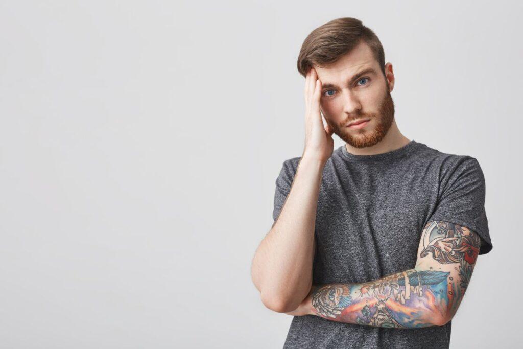 Tattooentfernung Düsseldorf als Ausweg: junger Mann mit farbigem Tattoo wirkt unsicher und zweifelnd