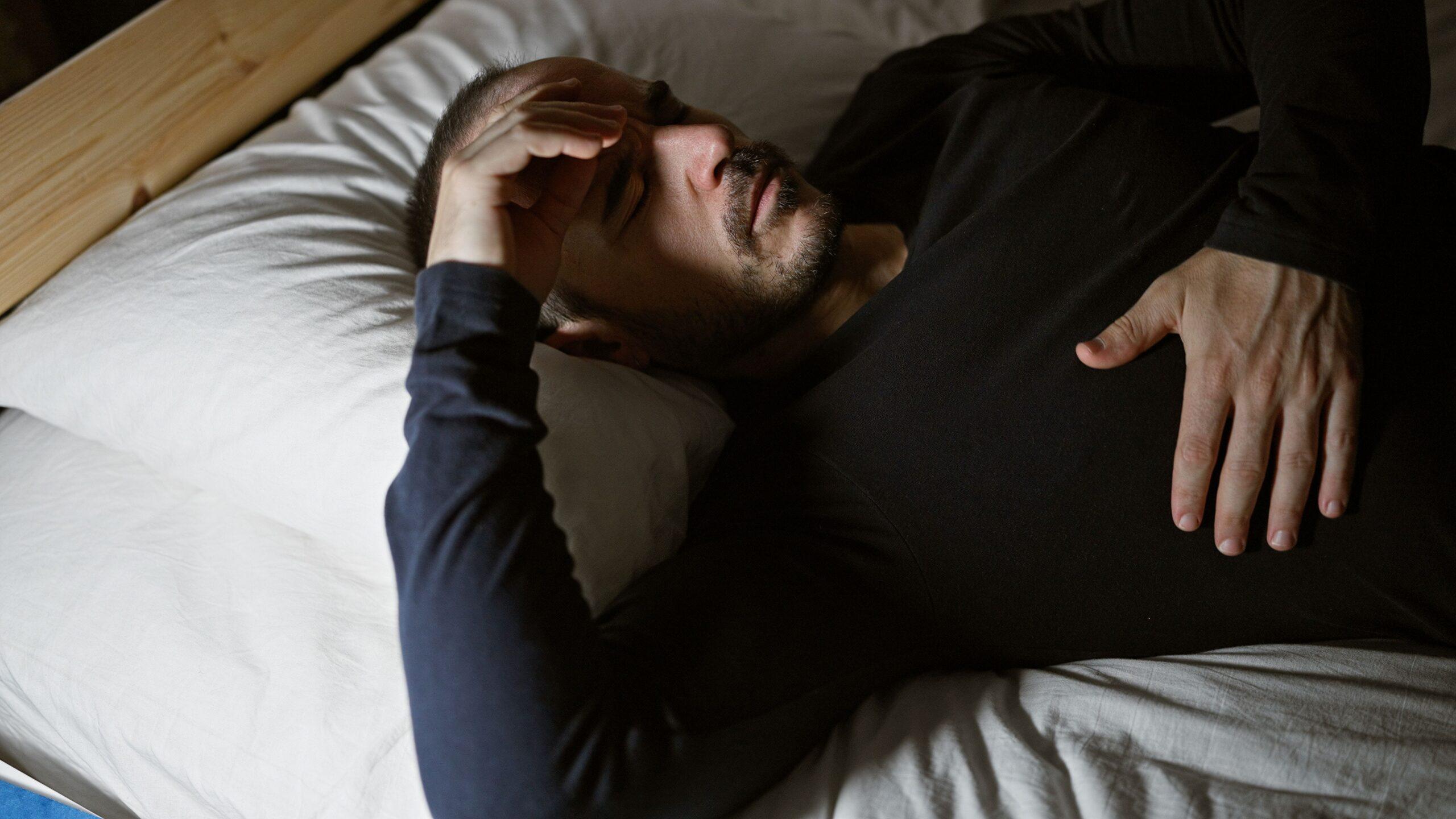Mann liegt unruhig im Bett mit der Hand auf der Stirn