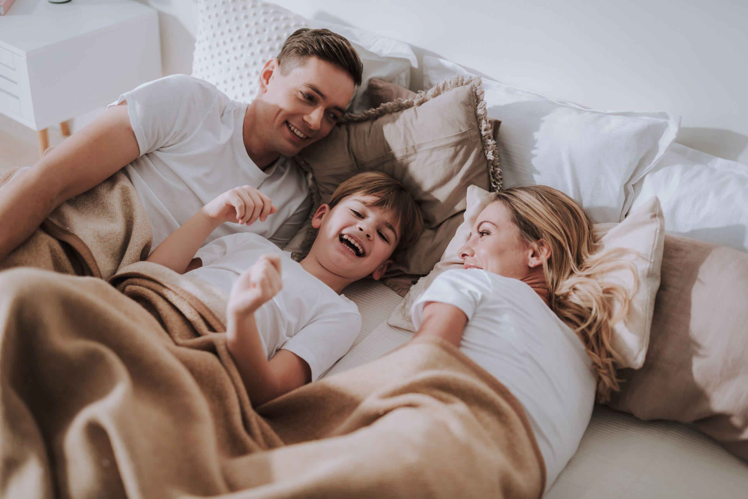 Glückliche Familie liegt gemeinsam im Bett – Entspannung und Schlafkomfort mit hochwertiger Bettwäsche