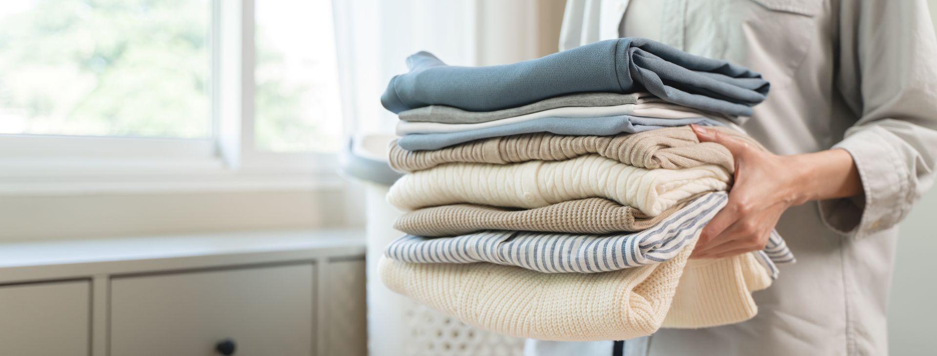 musselin kleidung und weitere sanfte stoffe ordentlich gefaltet in den armen einer person vor einem hellen fenster